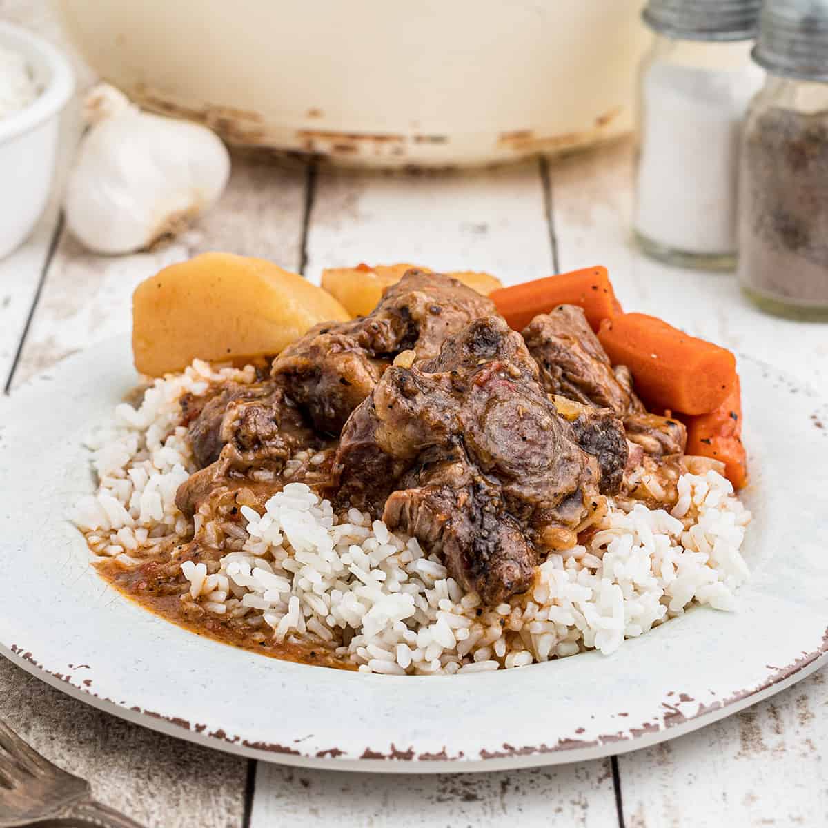 A serving of oxtail stew over rice on a dinner plate.