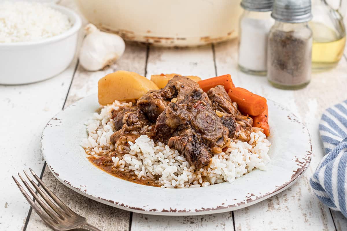 A serving of oxtail stew over rice on a dinner plate.