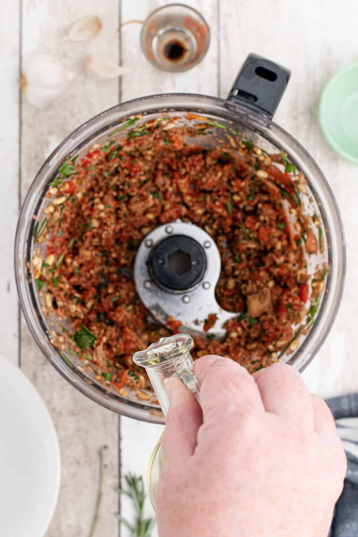 Drizzling olive oil into the sauce mixture in the food processor.