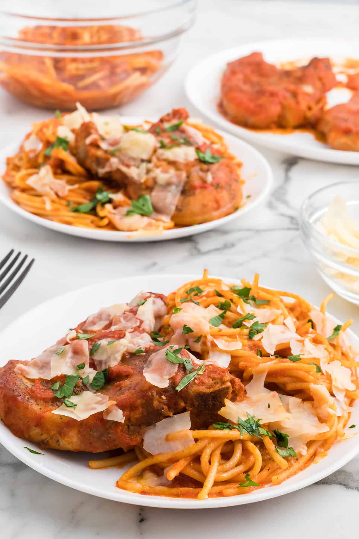 Plate of spaghetti with tomato sauce, pork chops, and shaved parmesan, garnished with parsley.