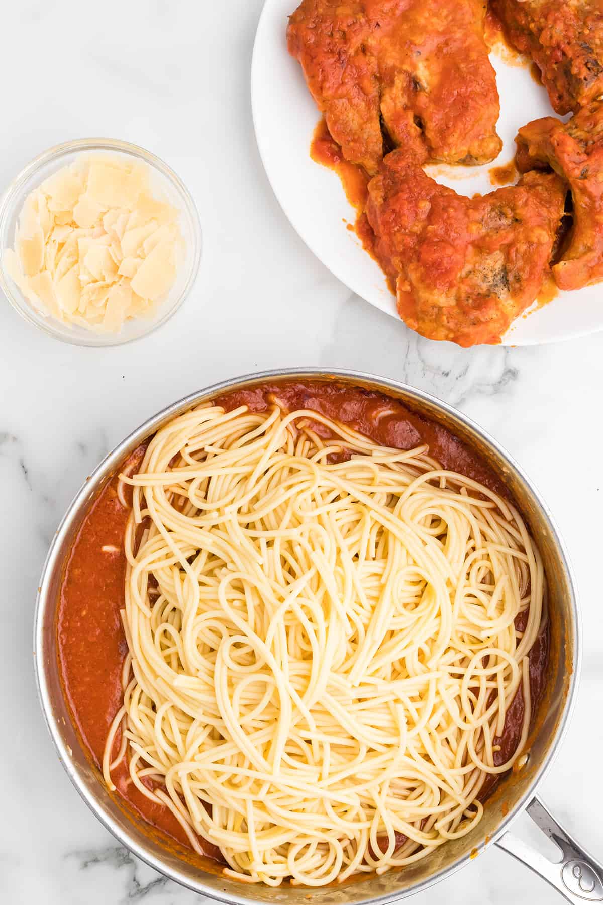 Drained spaghetti added to sauce in a skillet.