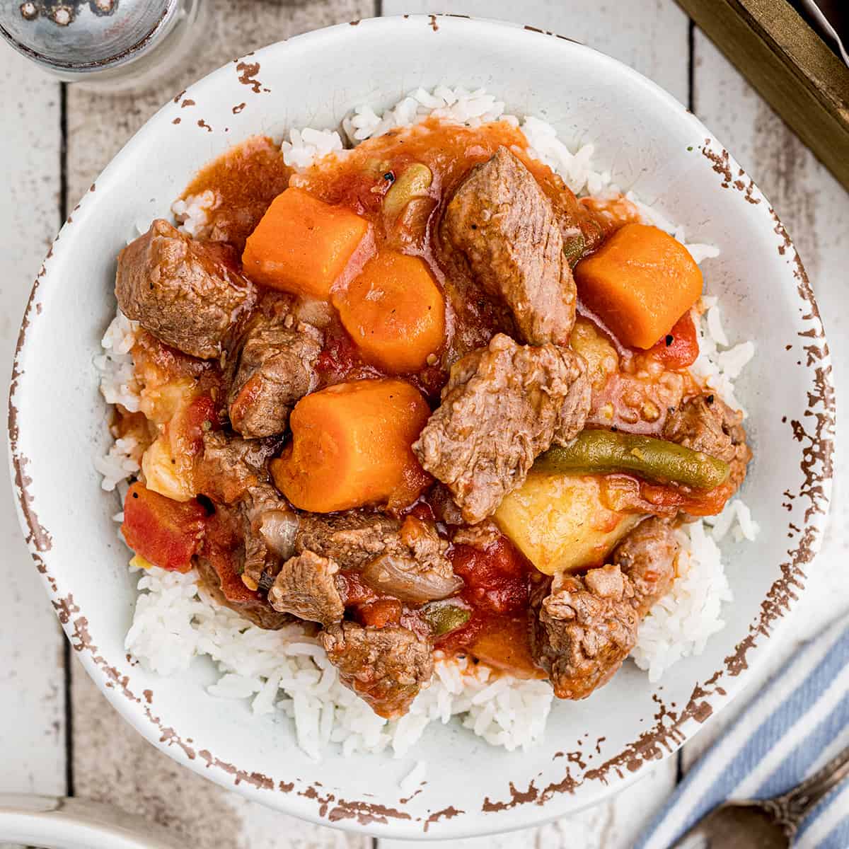 A serving of beef stew over rice in a white bowl.