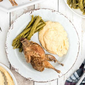 A serving of fried quail on a plate with cheese grits and asparagus.