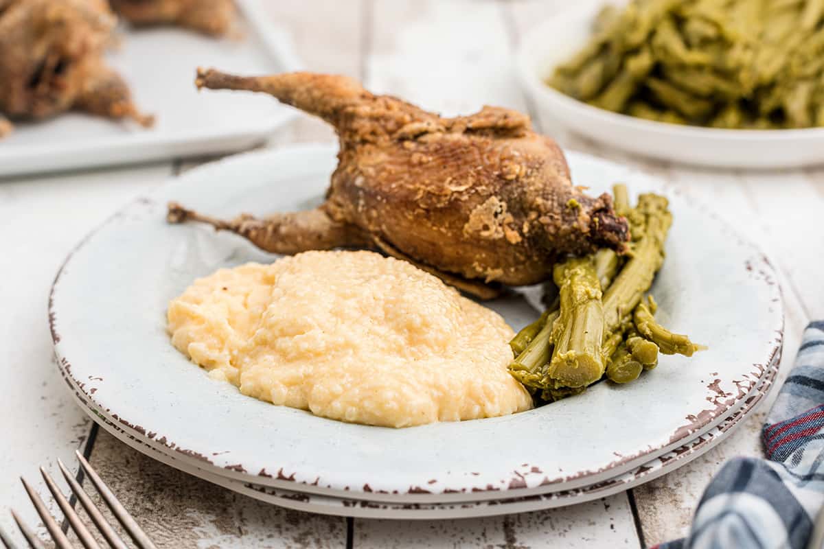 A serving of fried quail on a plate with cheese grits and asparagus.