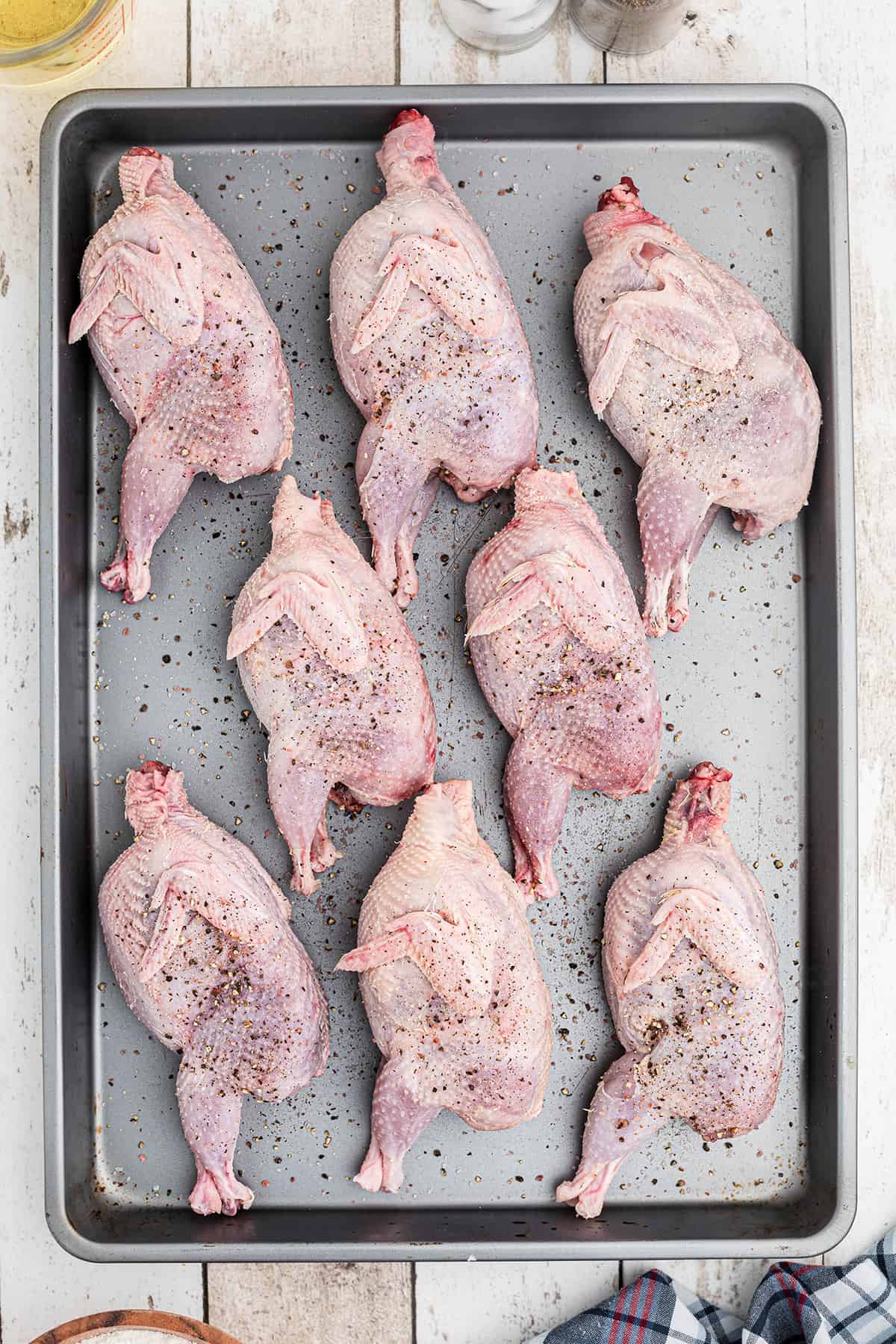 Seasoned quail on a baking sheet.