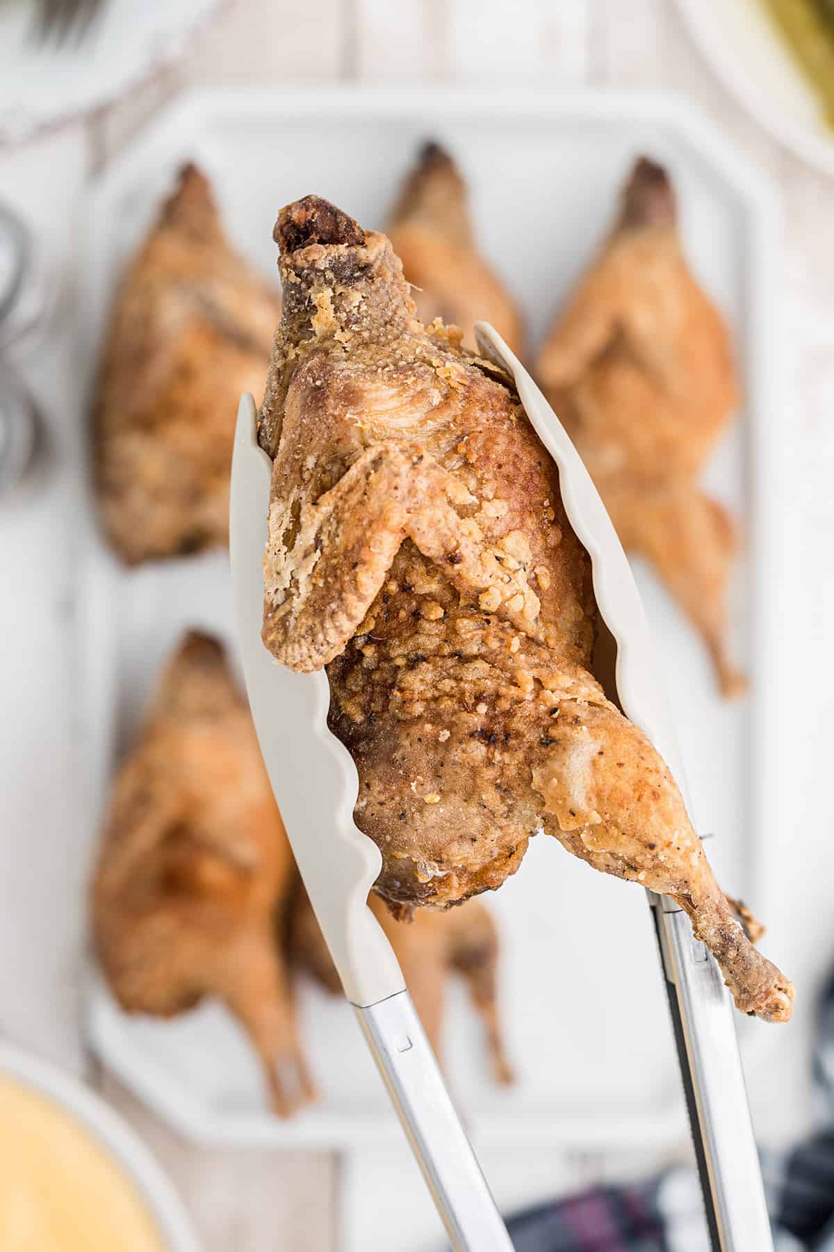 A single deep fried quail held in tongs.