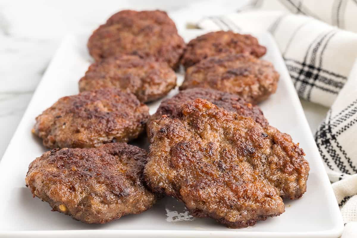 Cooked spicy pork sausage patties on a white plate.