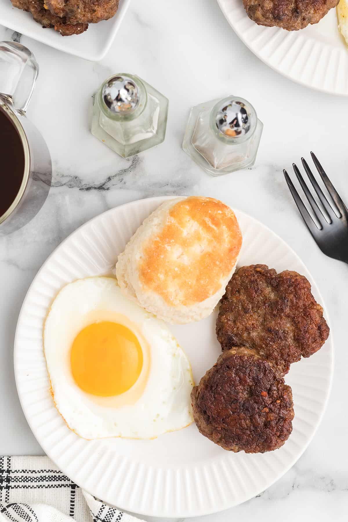 Sausage, a fried egg, and a biscuits on a plate.