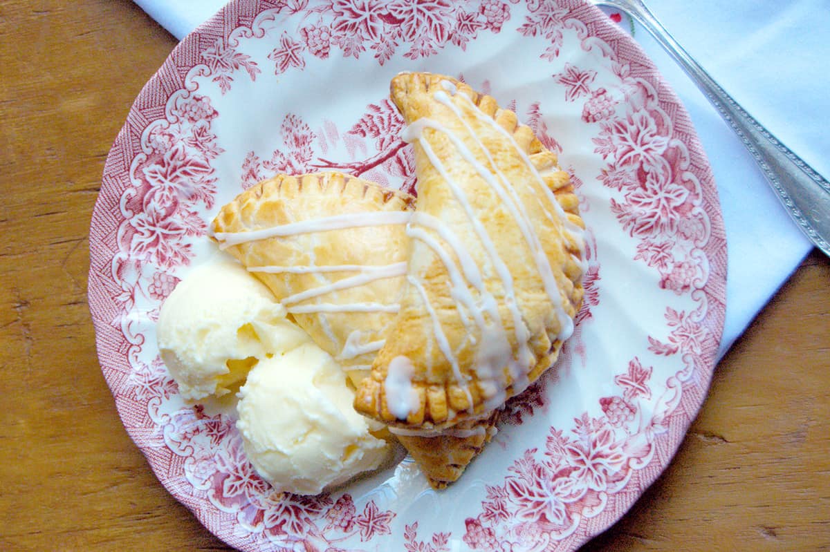 Two apple hand pies with vanilla ice cream on a serving plate.