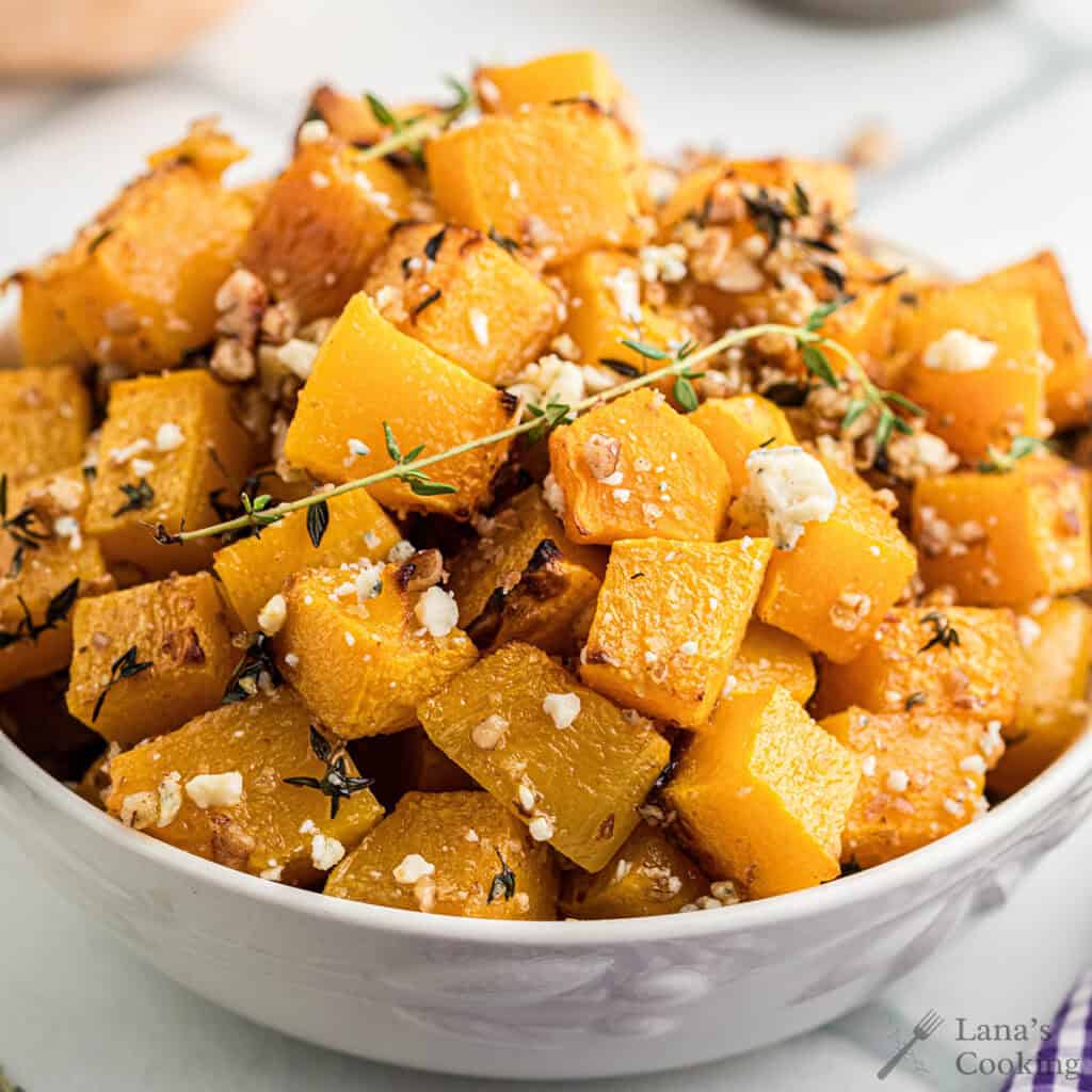 Baked butternut squash with blue cheese and pecans in a white serving bowl.