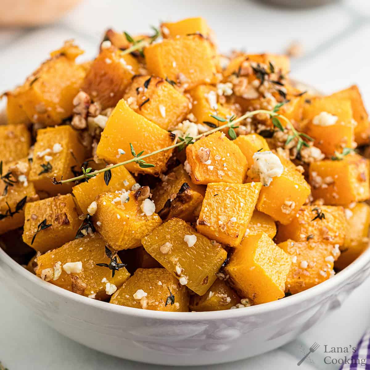 Baked butternut squash with blue cheese and pecans in a white serving bowl.