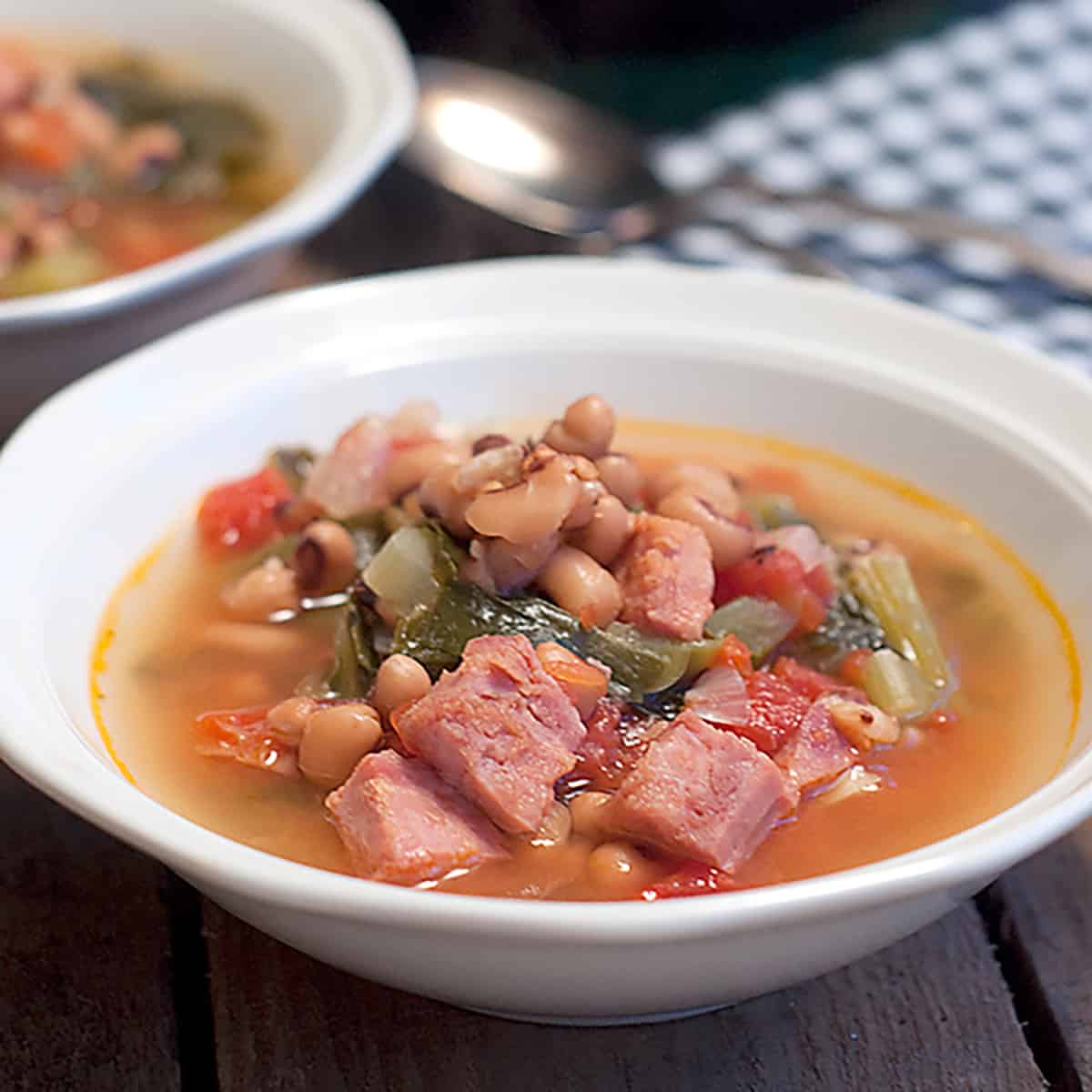 A serving of creole black eyed pea soup in a white bowl with a spoon on the side.