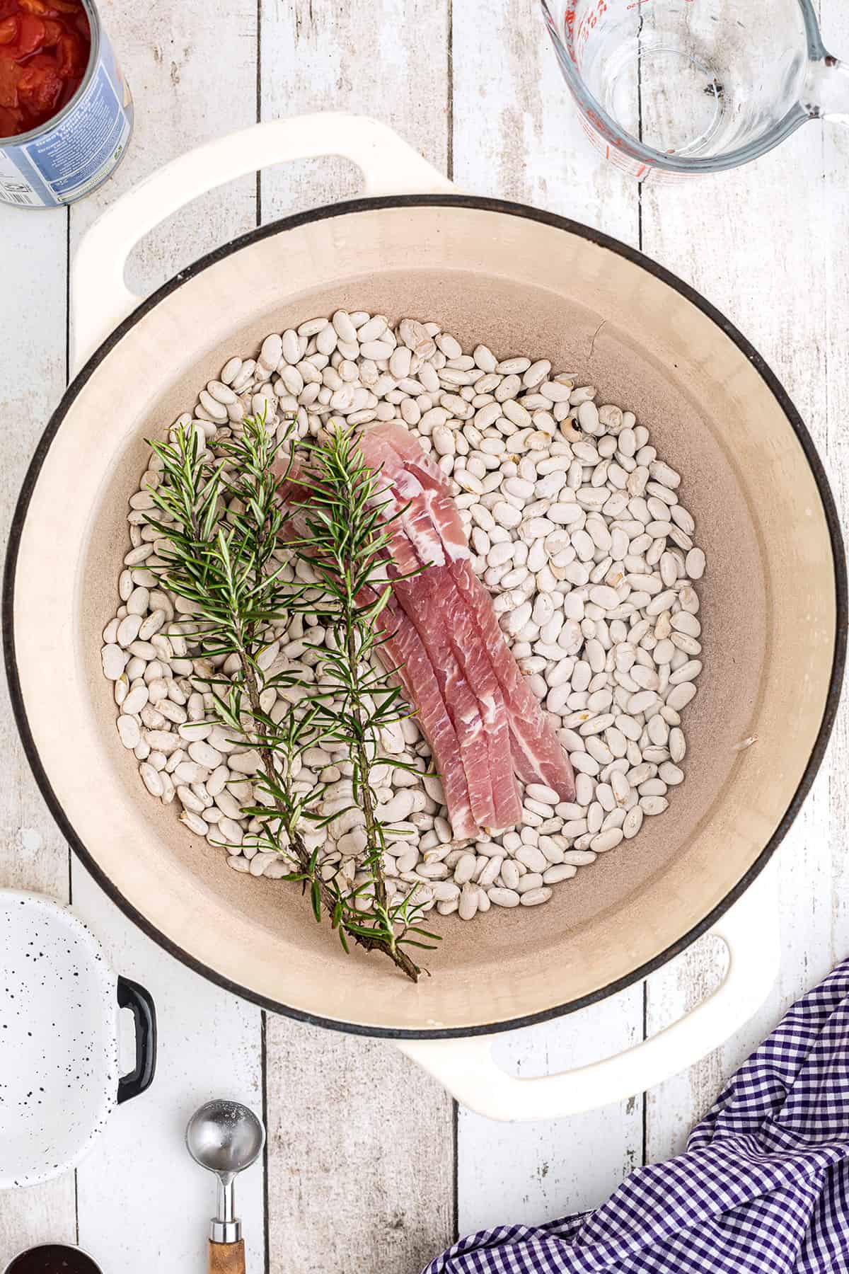 Beans, salt pork, and rosemary in a Dutch oven.