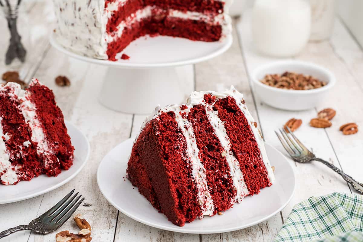 Finished red velvet cake with a slice held on a plate.