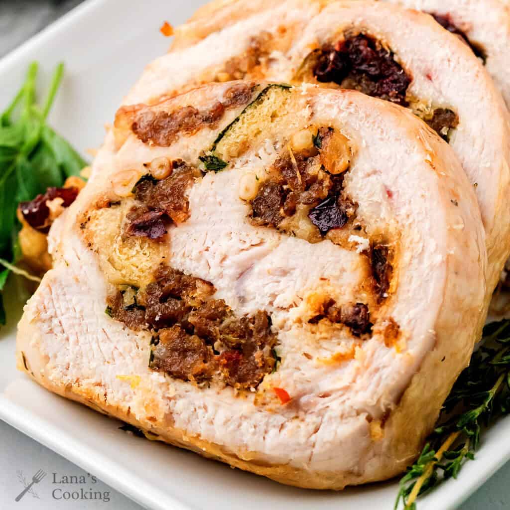 Sliced stuffed turkey breast with herbs and visible filling of bread, cranberries, and nuts on a white plate.