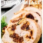 Sliced rolled turkey breast stuffed with bread, herbs, and cranberries on a white plate, garnished with greens.