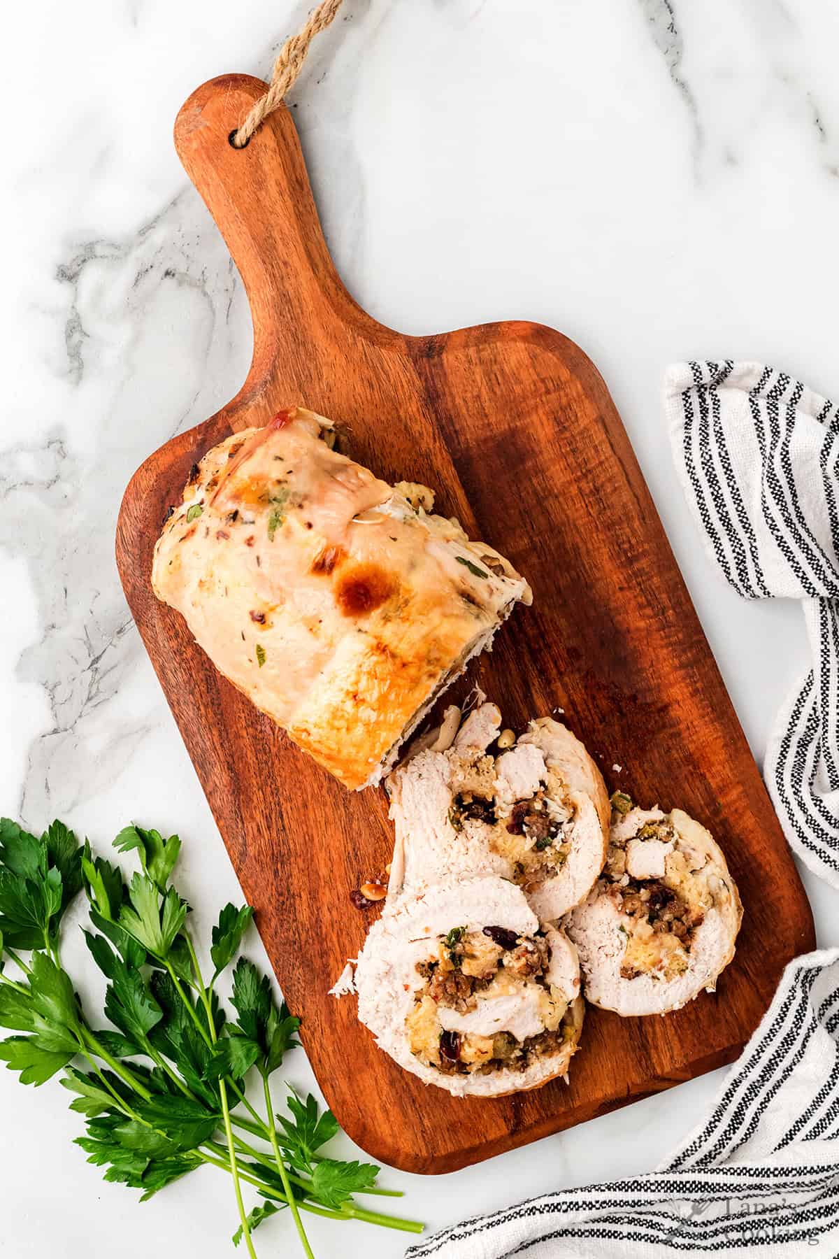 Sliced stuffed turkey breast on a wooden cutting board, garnished with parsley and a striped towel nearby.