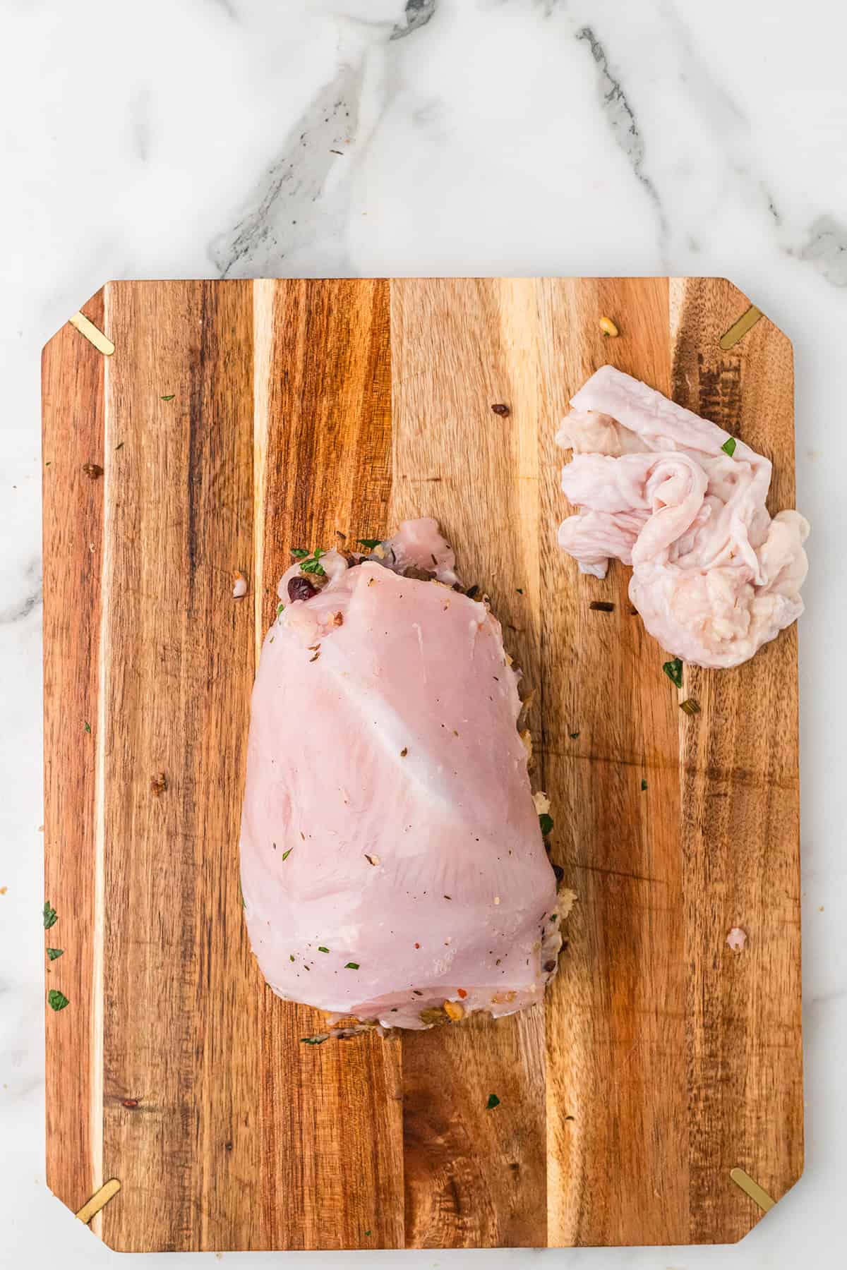Rolled and stuffed turkey breast and a small pile of turkey skin on a wooden cutting board, on a marble counter.
