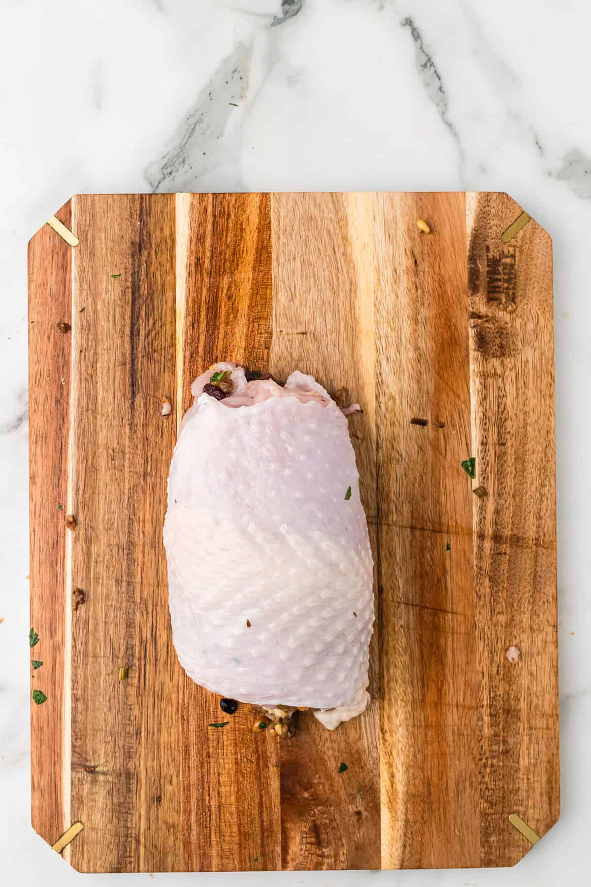 Raw, stuffed turkey breast on a wooden cutting board, placed on a white marble surface.