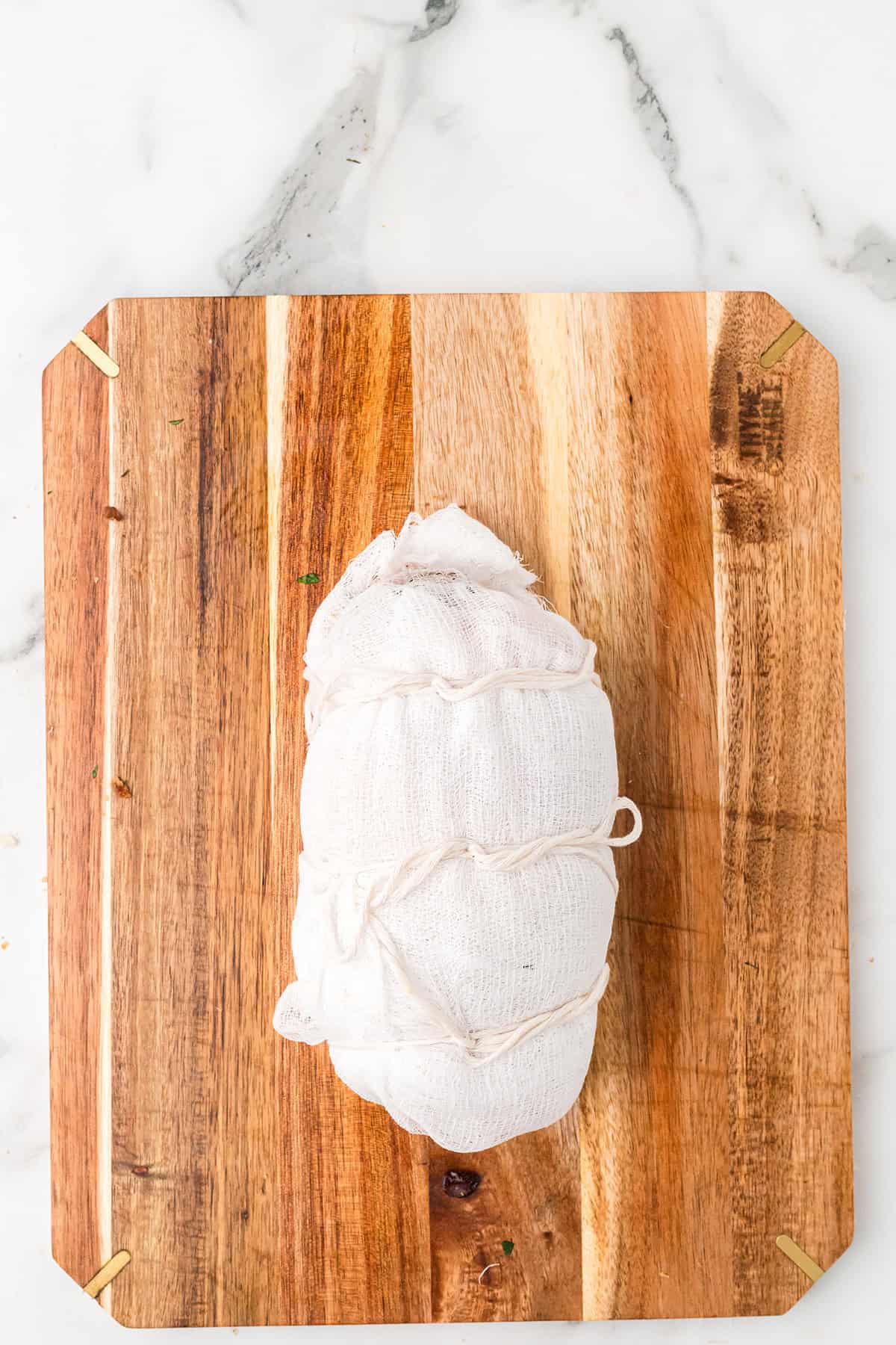 Rolled turkey breast wrapped in cheesecloth and tied with string on a wooden cutting board, marble surface background.