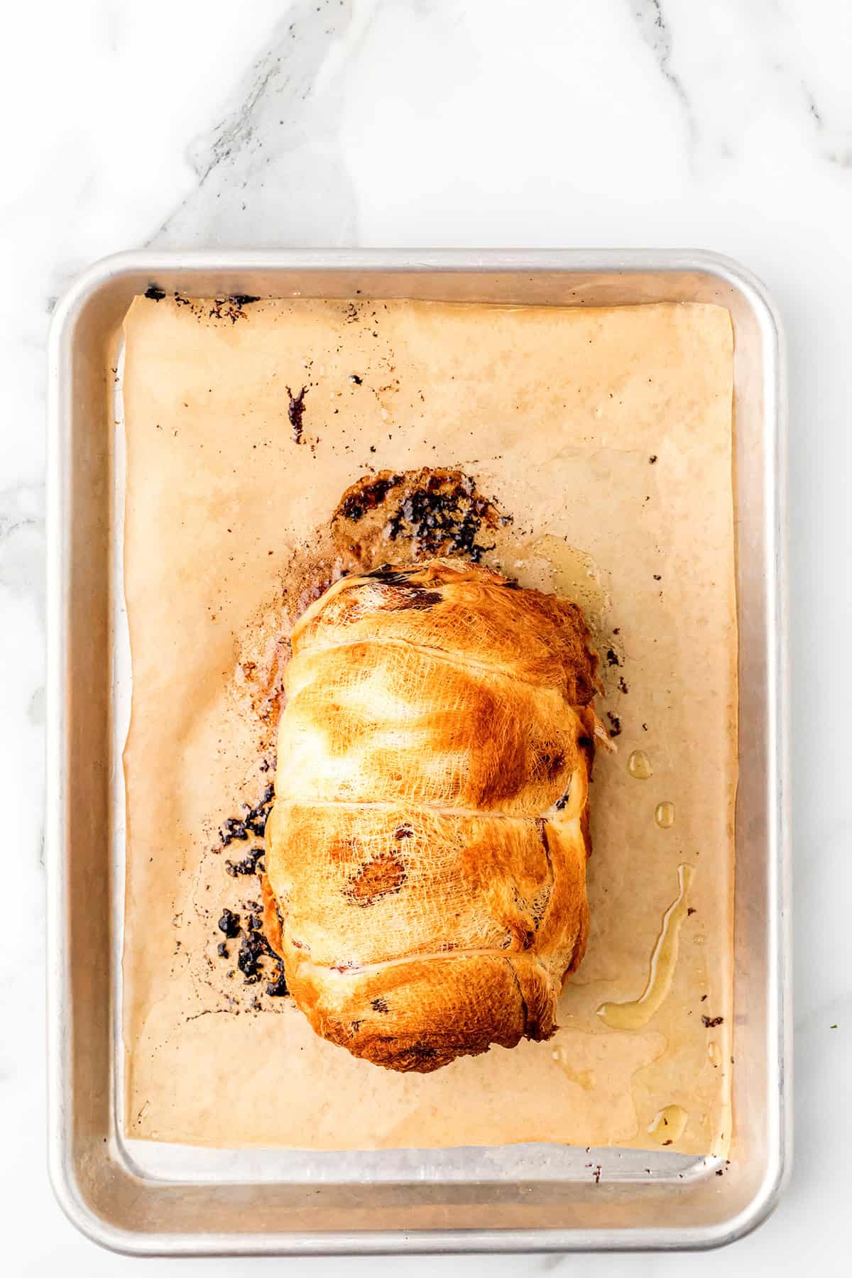 Golden-brown baked turkey breast on parchment-lined baking sheet, viewed from above on a marble surface.