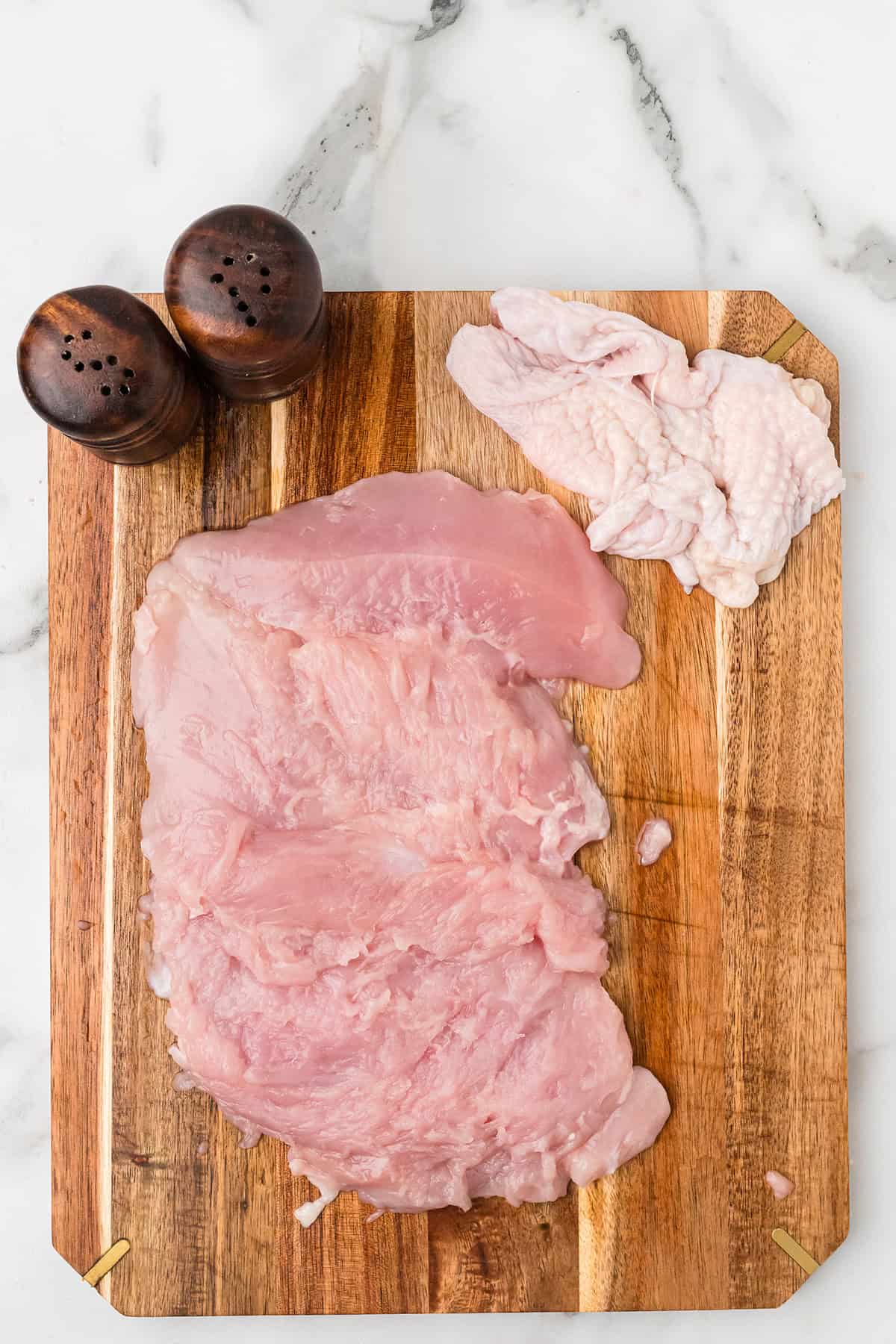 Raw turkey breast and skin on a wooden cutting board with salt and pepper shakers on a marble countertop.