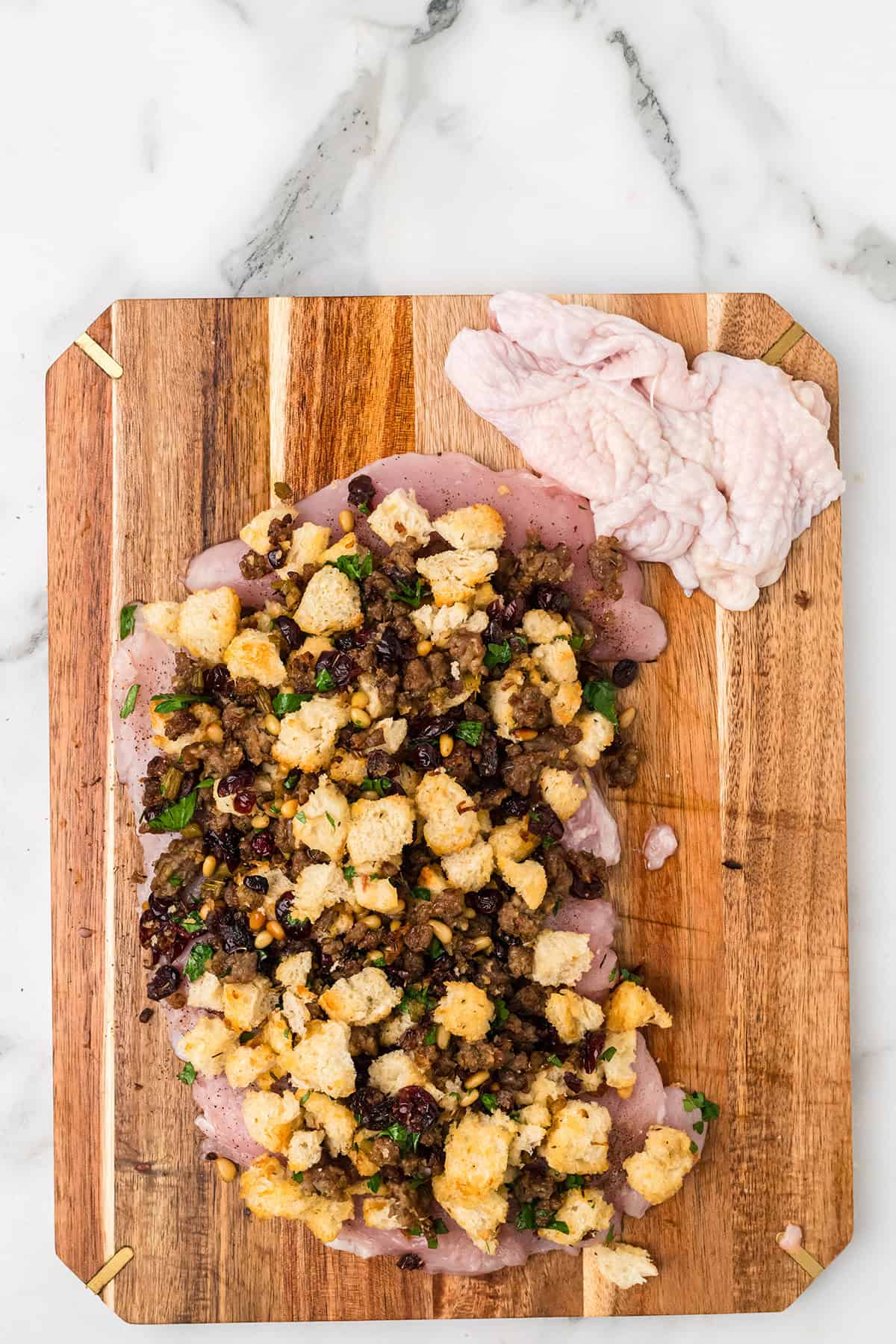 Uncooked turkey breast on a cutting board topped with stuffing, with extra skin set aside.