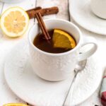 A cup of spiced tea with a lemon slice and a cinnamon stick in the cup.