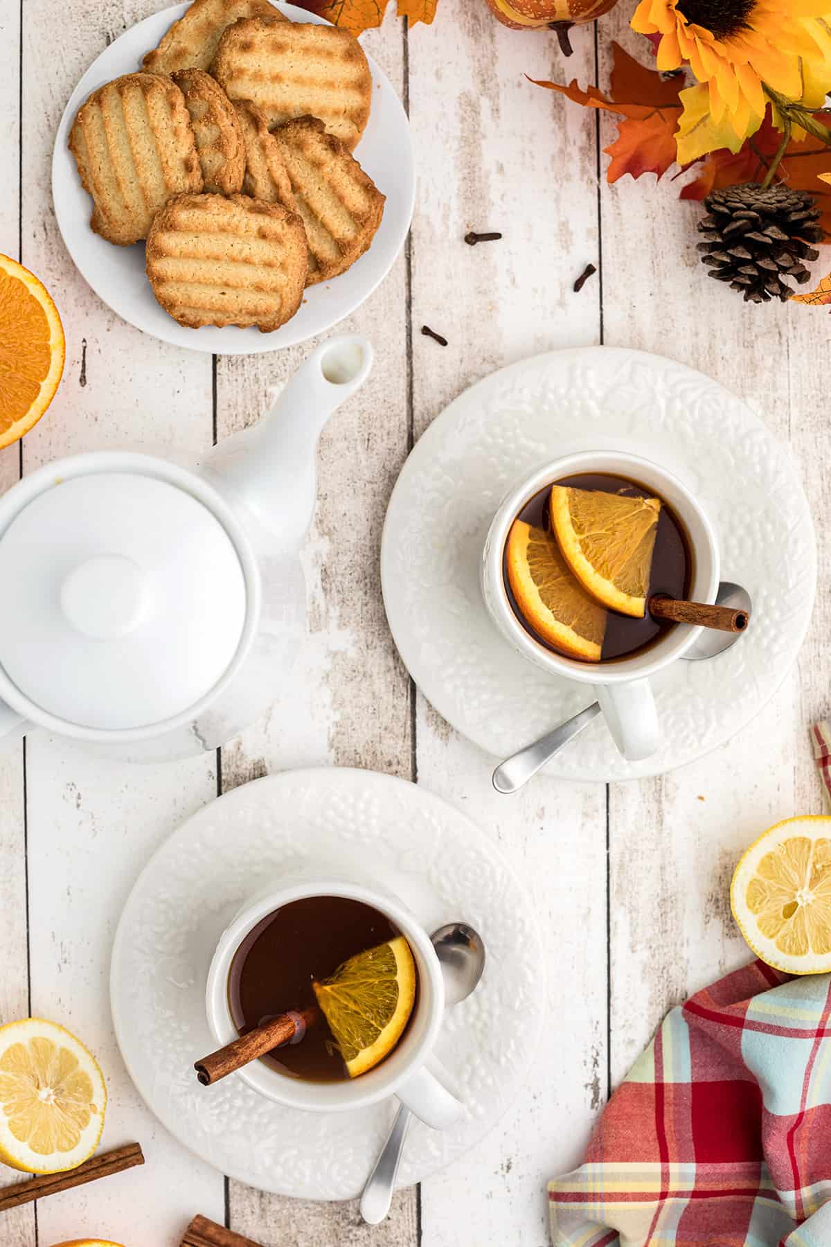 Two cups of spiced tea with a plate of cookies in the background.