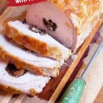 Sliced stuffed pork loin with apricots and prunes on a wooden cutting board, knife beside it.