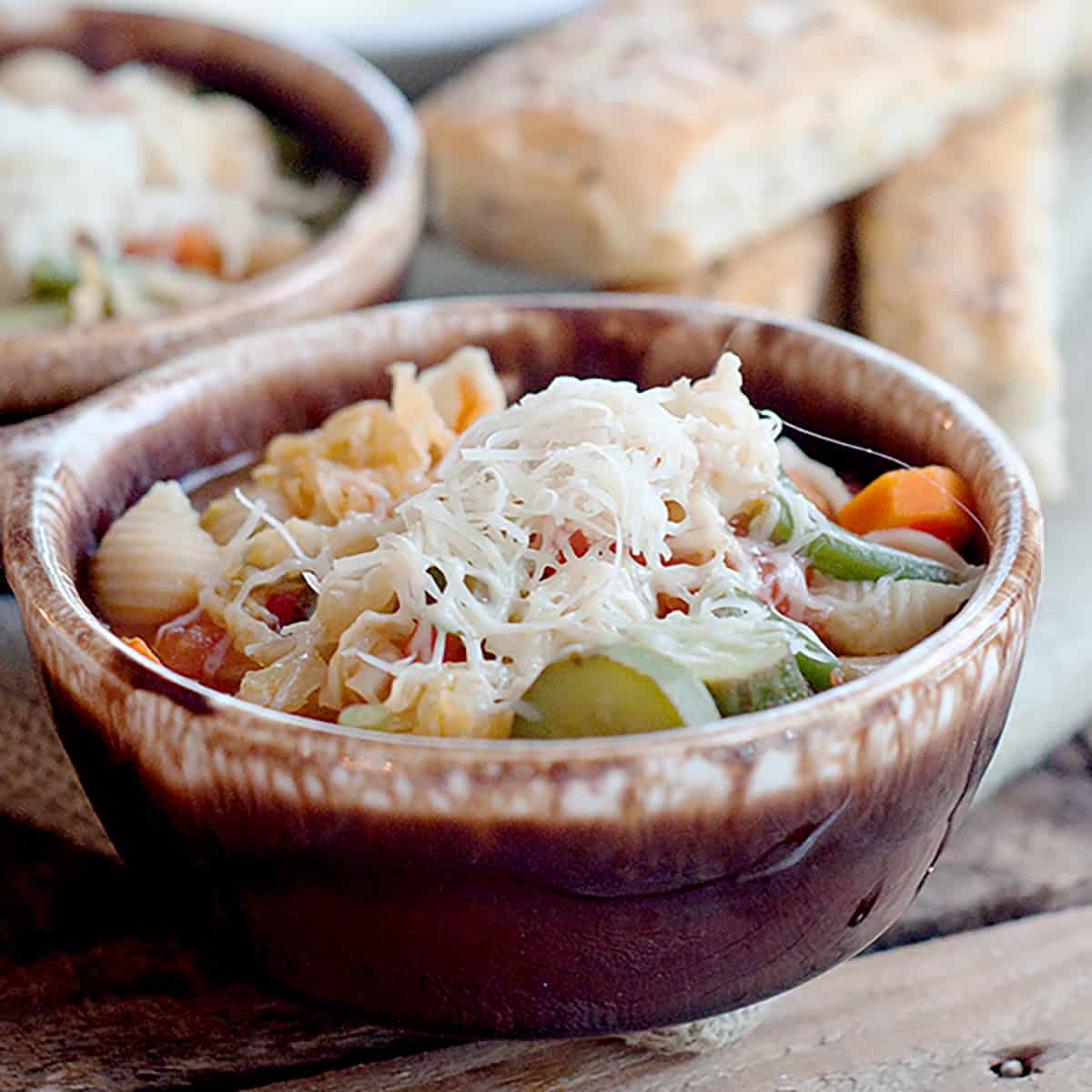 Minestrone topped with grated cheese in a brown bowl.