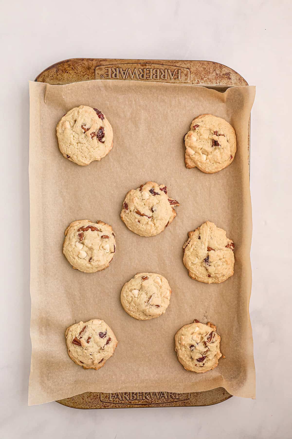 A baking tray lined with parchment paper holds eight freshly baked cookies spaced apart.