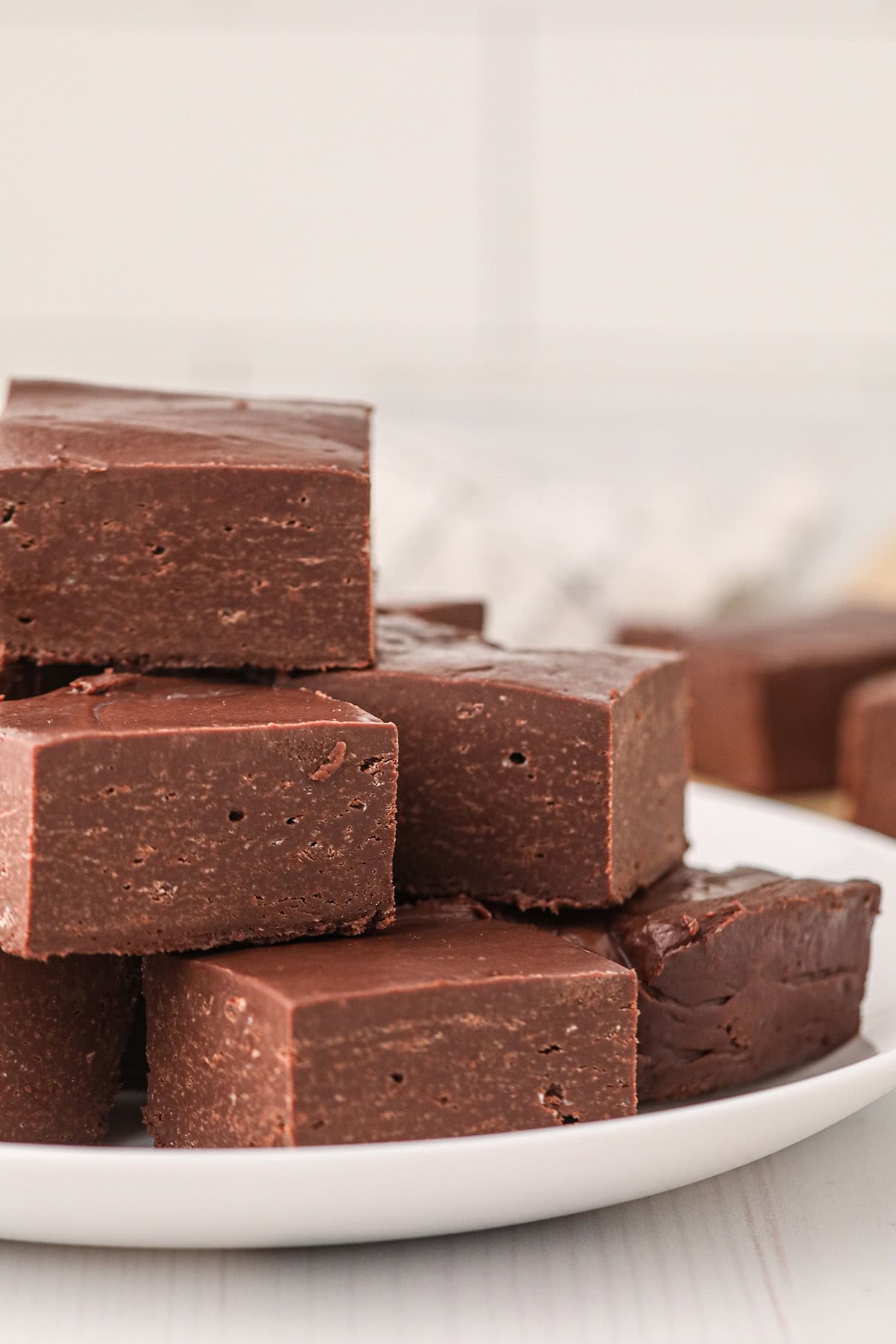 A stack of thick, square pieces of chocolate fudge on a white plate.
