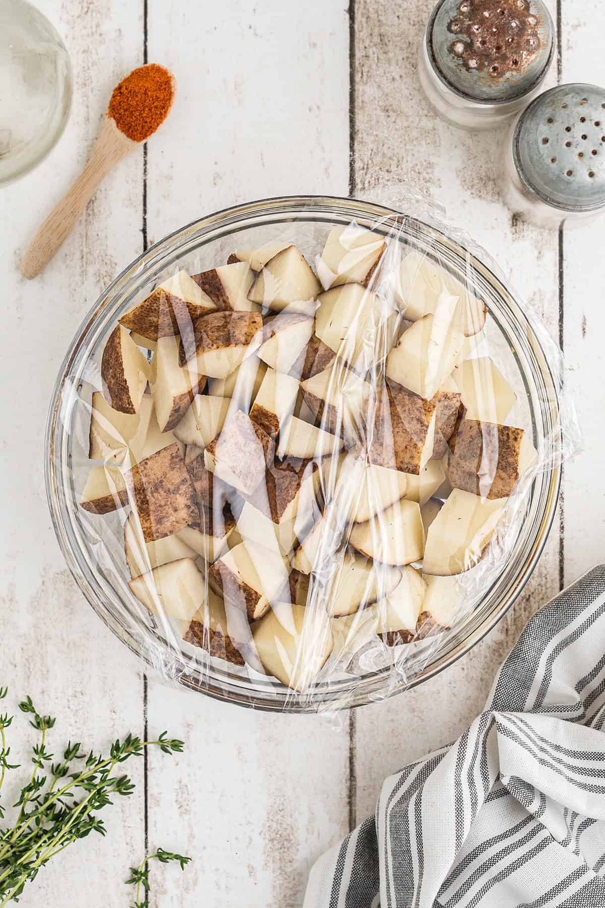 Potatoes in a glass bowl covered with plastic wrap.