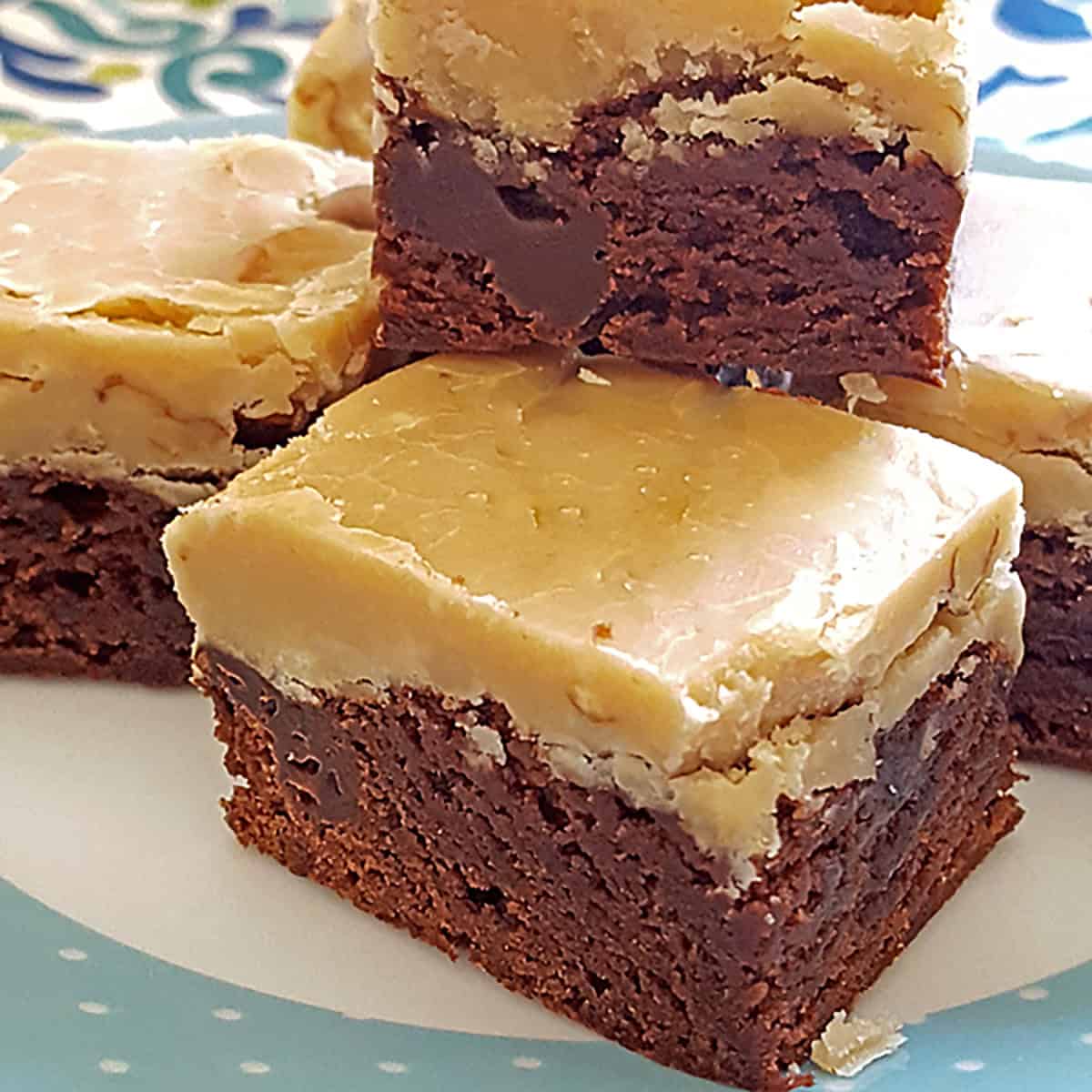 Fudgy chocolate brownies with a thick layer of creamy praline, stacked on a decorative plate.
