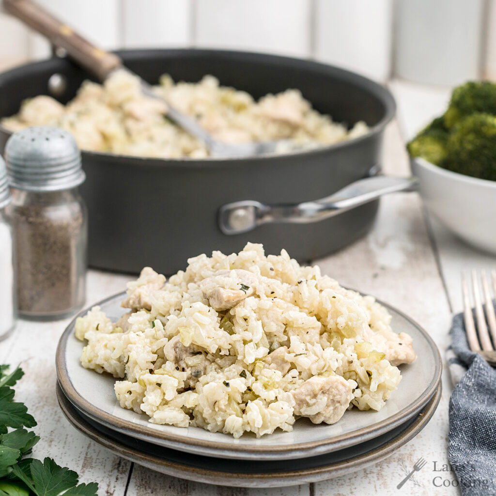 A serving of chicken and rice on a dish with a skillet in the background.