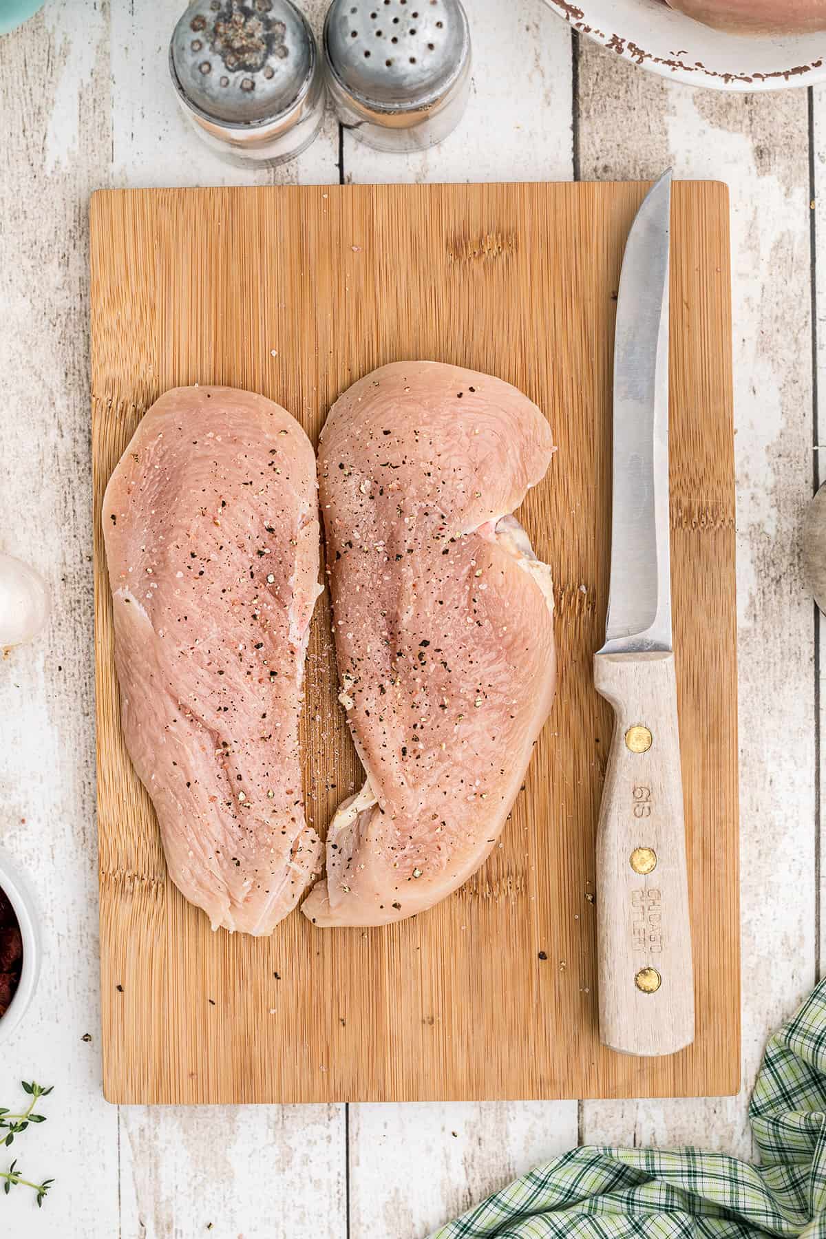Raw chicken breasts and a knife on a wooden board.