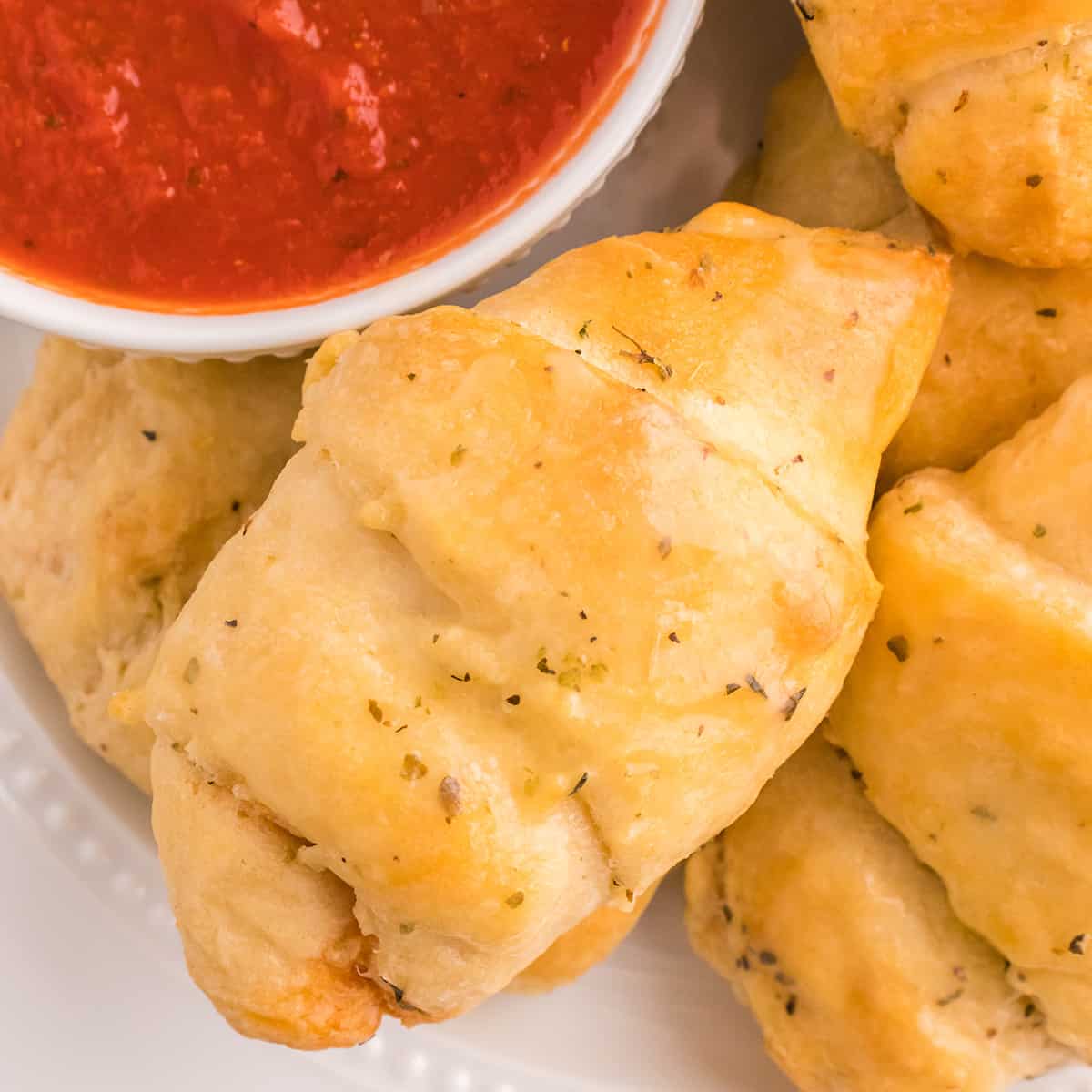 Pizza rolls on a plate with a dish of pizza sauce.