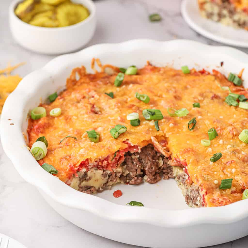 Cheeseburger pie in a white dish with one slice missing.