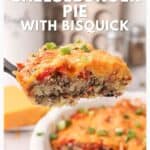 A slice of cheeseburger pie topped with cheese and green onions on a serving spatula above a pie dish.
