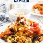 A plate of chicken country captain with rice, raisins, almonds, and vegetables, topped with sauce.