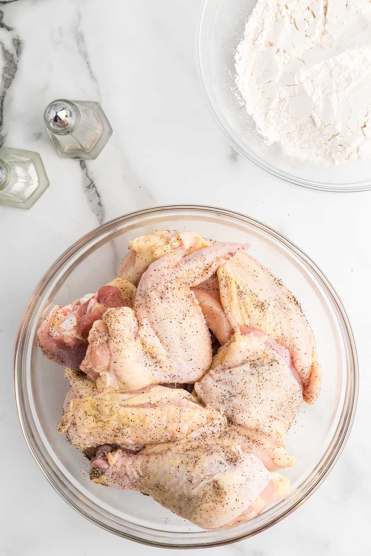 Chicken seasoned with salt and pepper in a bowl.