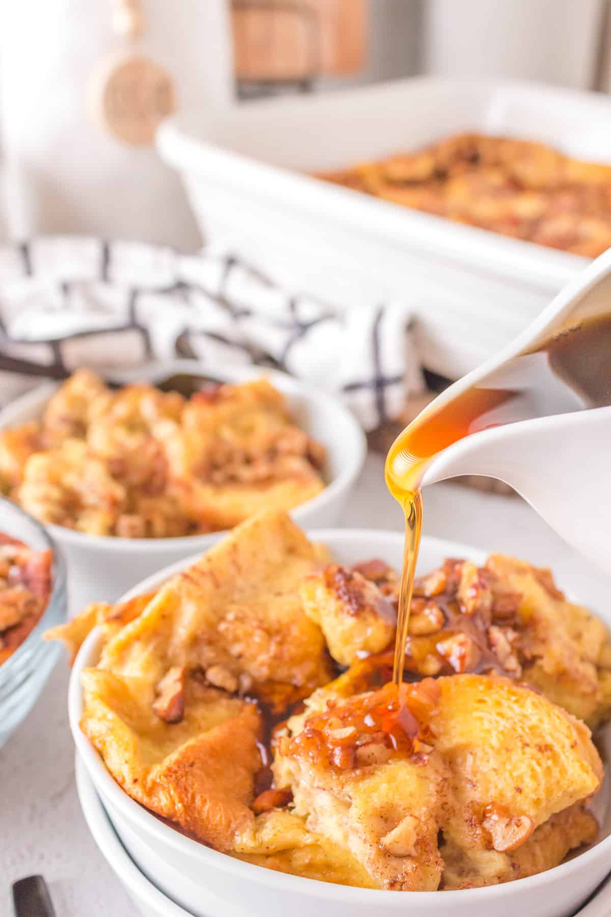 A serving of french toast casserole with syrup being poured from a pitcher.