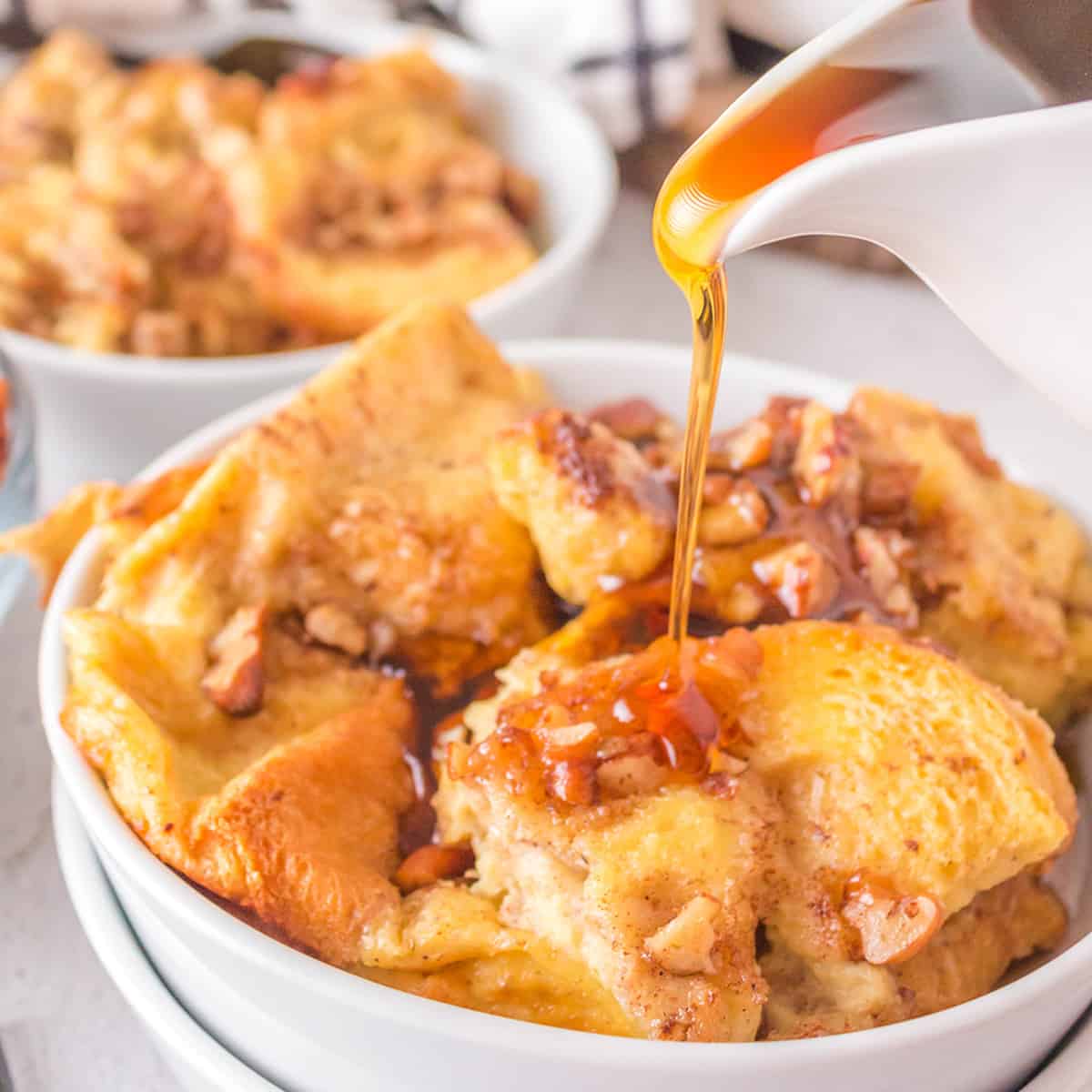 A serving of french toast casserole with syrup being poured from a pitcher.