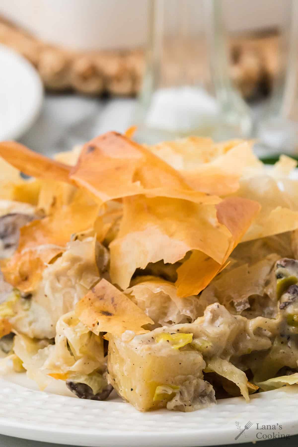 A close-up of a savory casserole topped with crispy, golden-brown phyllo pastry on a white plate.