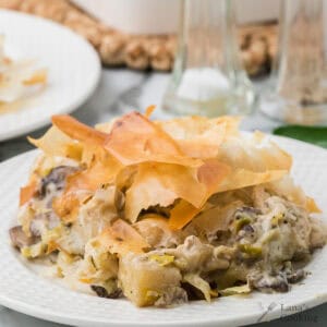 Creamy chicken, leek, and mushroom pie topped with crispy golden phyllo pastry on a white plate.