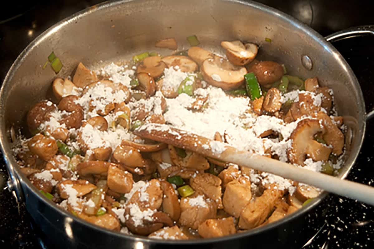 Flour added to the chicken in a skillet.