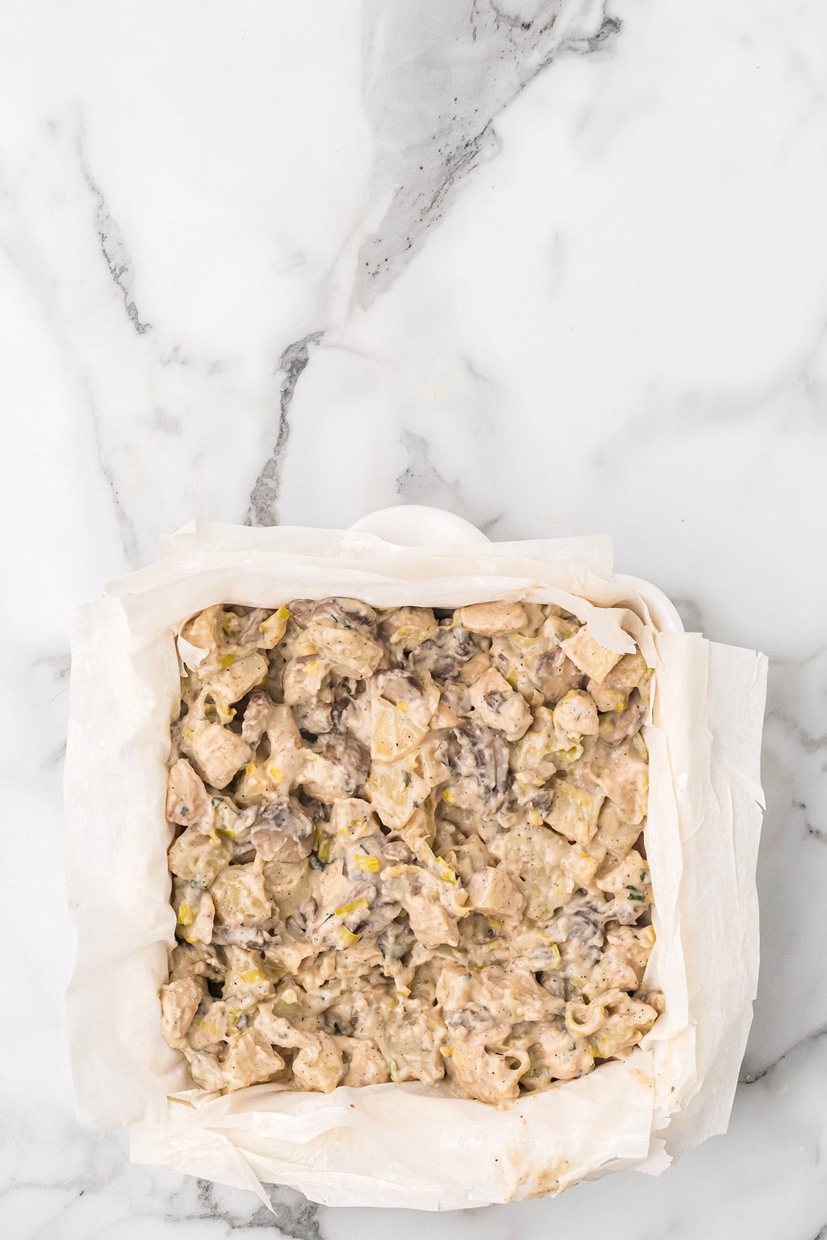 Unbaked casserole mixture in a phyllo-lined square baking dish on a white marble surface.