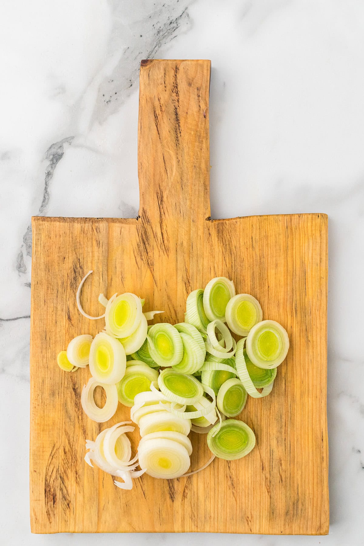 Sliced leeks on a wooden cutting board set on a white marble surface.