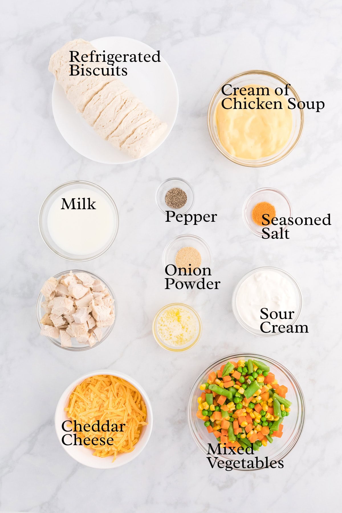 Assorted ingredients in bowls for a casserole, including biscuits, soup, cheese, chicken, vegetables, and seasonings.